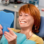 Older woman looking at smile in mirror in dental chair