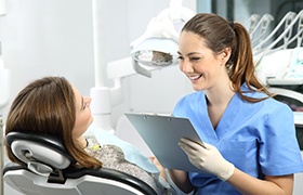 Dental receptionist smiling while taking notes on clipboard