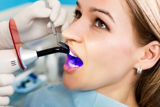 Closeup of gloved hands applying UV light to woman’s dental treatment 