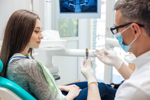 Dentist showing large model dental implant to woman in dental chair