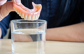 a person putting a denture in a glass of water