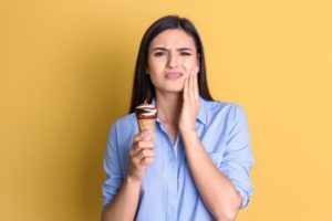 young woman eating ice cream and holding her face because of tooth sensitivity 