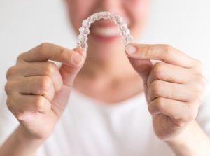 Smiling woman holding Invisalign in Beverly in front of her