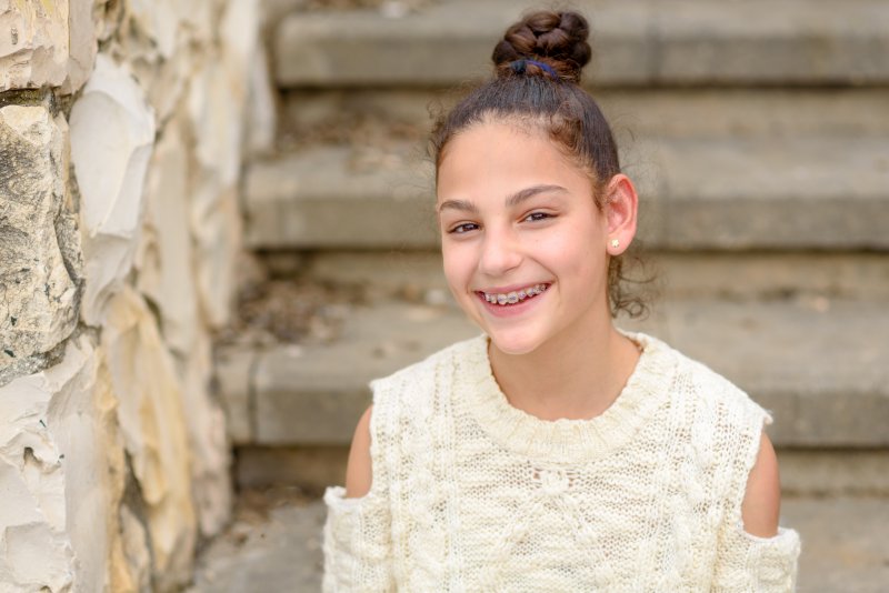 Child with braces smiling on steps