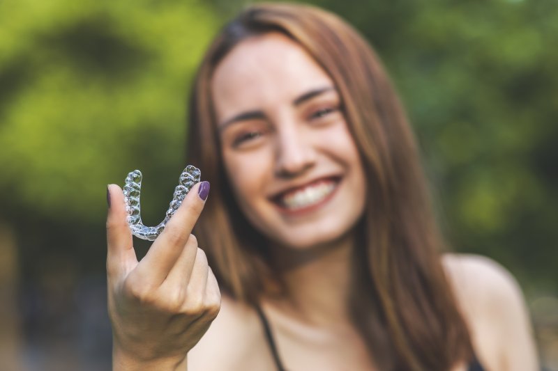 person correcting bite problems with Invisalign holding tray and smiling